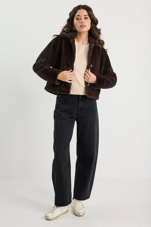 Woman wearing a brown jacket, beige top, black pants, and white sneakers on a white background