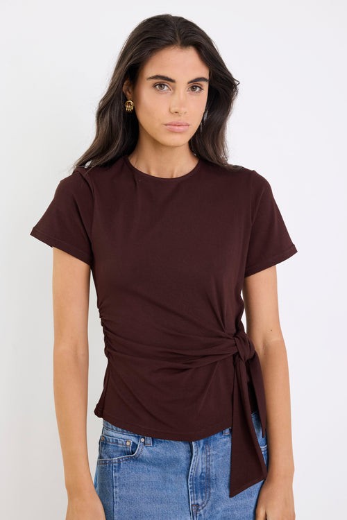 Woman wearing a brown t-shirt with a tie detail and blue jeans on a white background