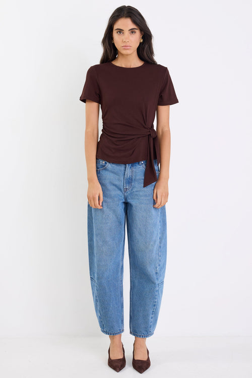 Woman wearing a brown top and blue jeans on a white background