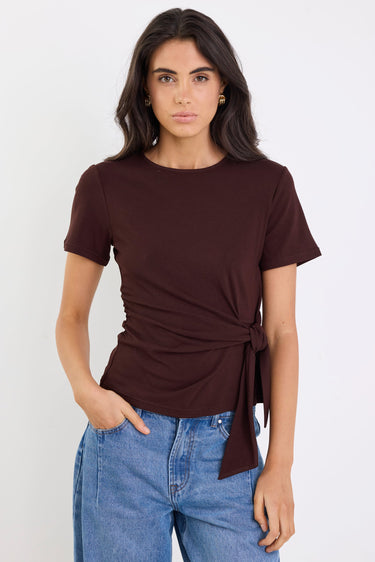 Woman wearing a brown tie-front top and blue jeans against a white background