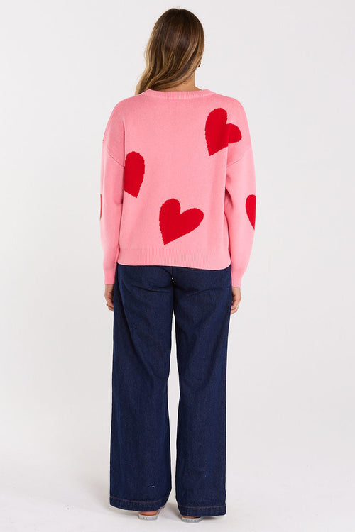 Person wearing a pink sweater with red heart patterns on a white background