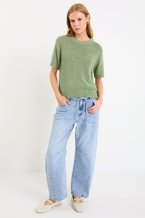 Woman wearing a green sweater and light blue jeans on a white background