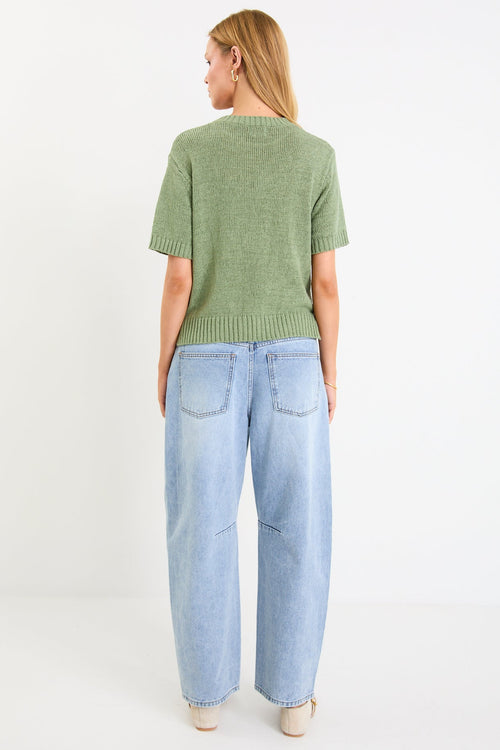 Person wearing a green sweater and light blue jeans on a white background