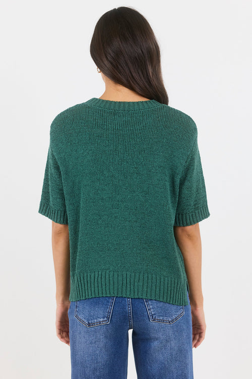 Person wearing a green knitted sweater and blue jeans on a white background