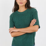 Woman wearing a green sweater and blue jeans against a white background