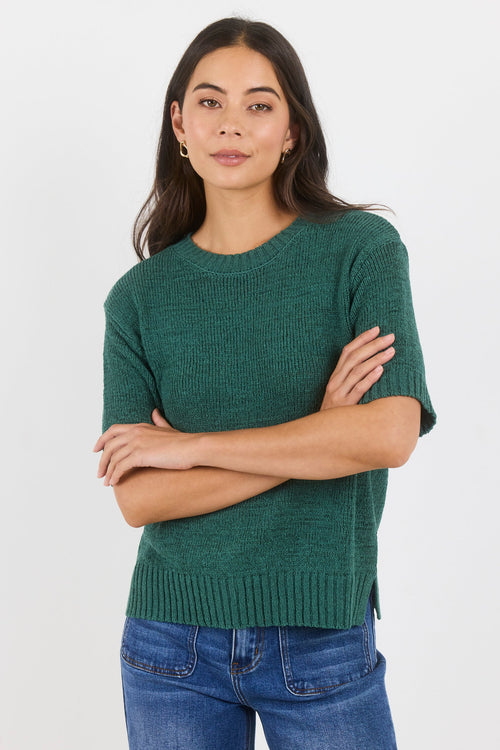Woman wearing a green sweater and blue jeans against a white background