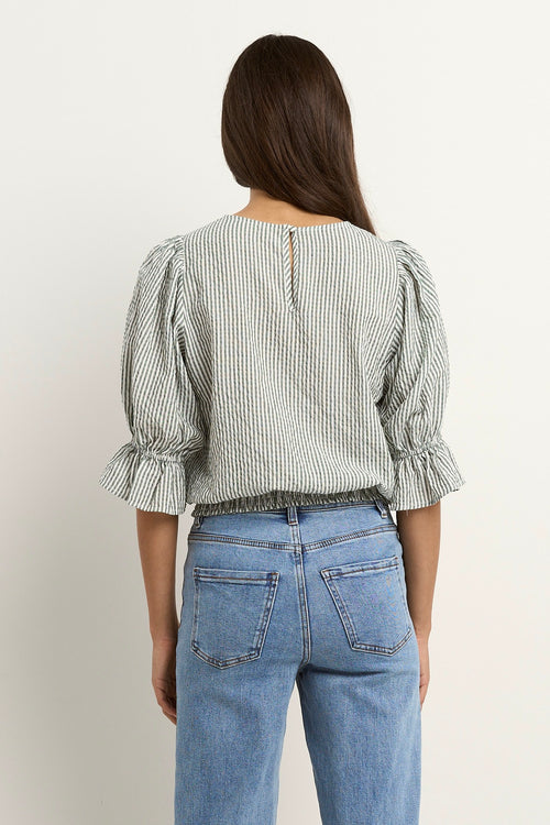 Woman wears a khaki and white striped puff sleeve top with frill detail, paired with light denim jeans.