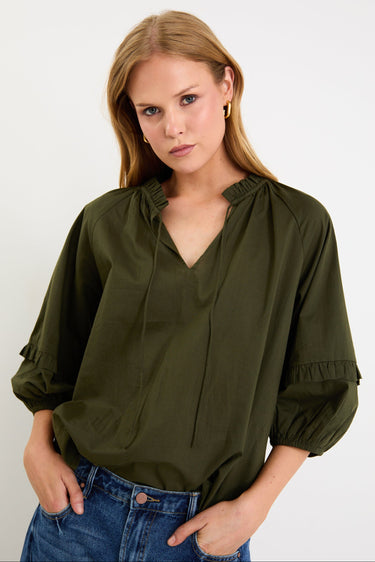 Woman wearing an olive green blouse with a plain background