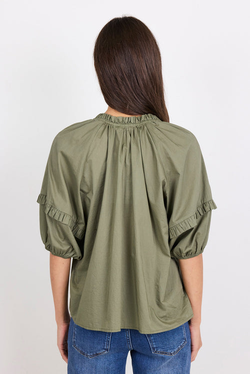 Woman wearing an olive green blouse with ruffled sleeves on a white background