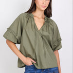 Woman wearing an olive green blouse with ruffled sleeves and blue jeans on a white background