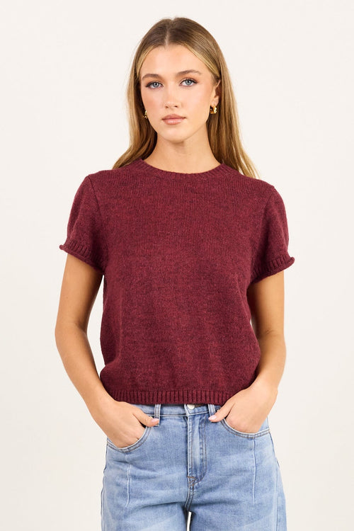 A woman modeling a short-sleeve maroon knit top and light-wash wide-leg blue jeans against a plain off-white studio background.