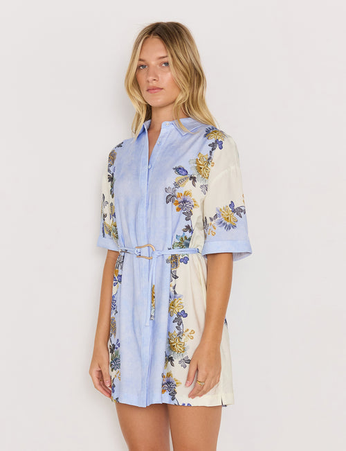Woman wearing a floral dress with a light blue shirt over it on a white background