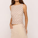 Woman wearing a patterned sleeveless top and beige skirt against a plain background