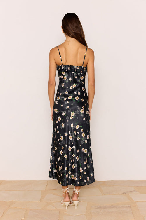 Woman wearing a black floral dress against a white wall.