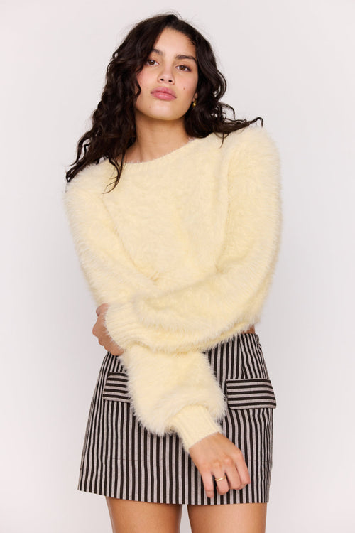 Woman wearing a light yellow fluffy sweater and striped skirt against a white background