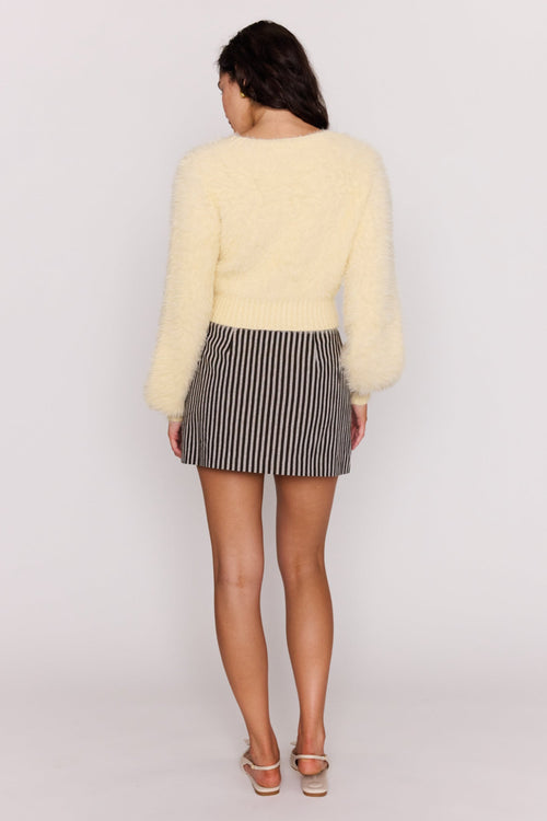 Person wearing a light yellow sweater and striped skirt on a white background