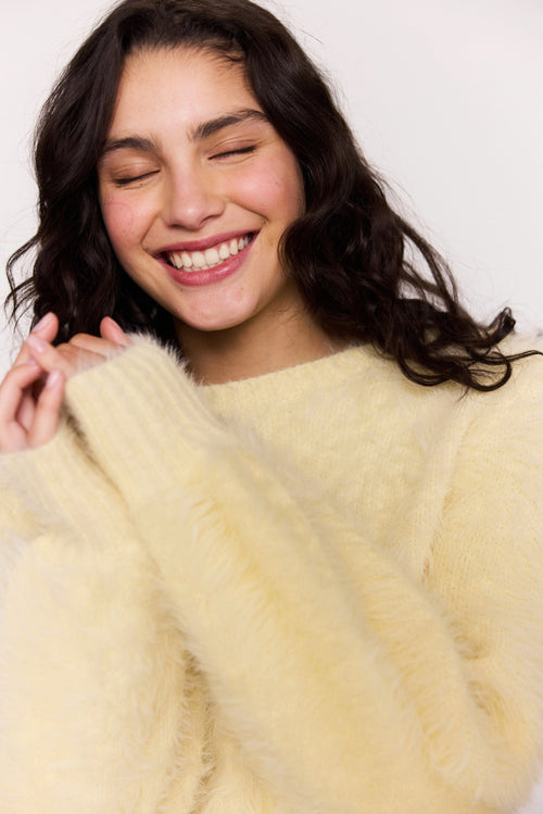 Woman wearing a light yellow fluffy sweater against a white background