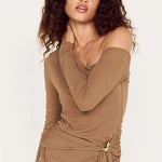 Woman wearing a brown top with a tie detail and blue jeans on a white background