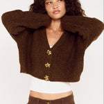 Woman wearing a brown cropped sweater with gold buttons on a white background