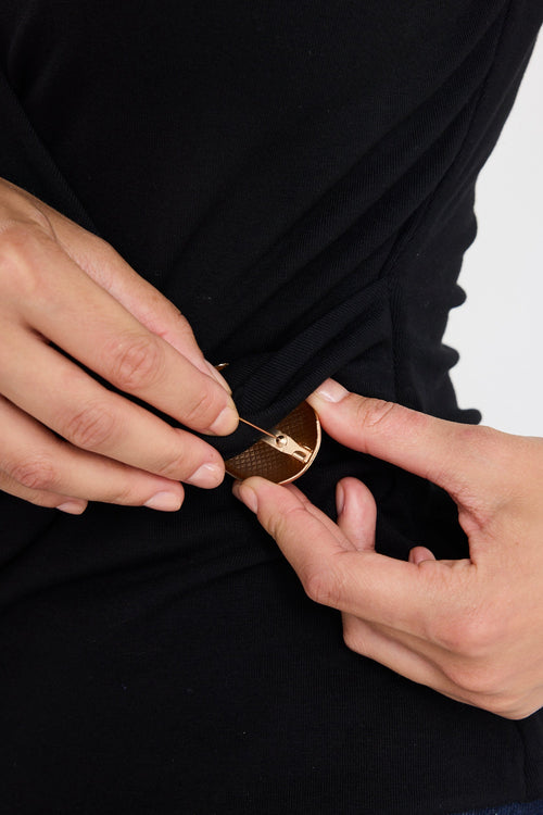 Person adjusting a gold belt buckle on a black shirt against a white background