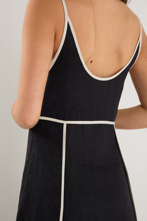 Woman wearing a black linen strappy dress with white contrast trim, fully lined, styled with black heeled sandals.