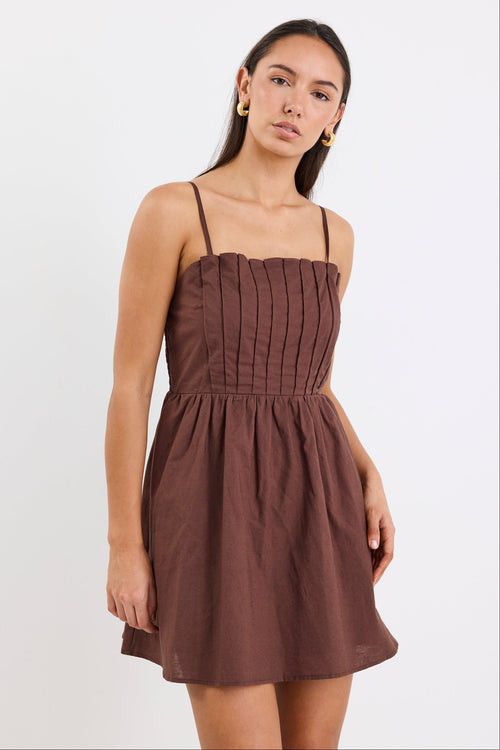Woman wears a chocolate brown mini dress with pleated bodice