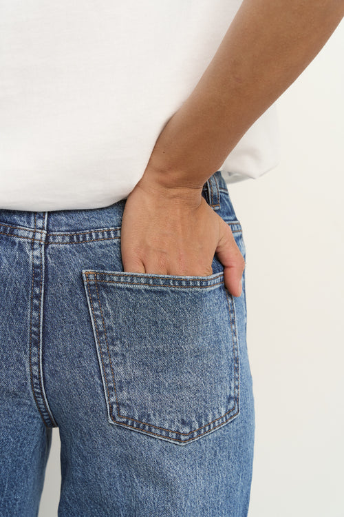 Woman wearing high rise, wide leg classic blue jeans with front seam detail, styled with a white tee and white sneakers.