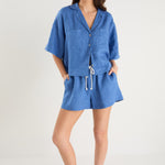 Woman wearing high-rise cornflower blue linen pull-on shorts with rope tie detail, styled with a blue shirt