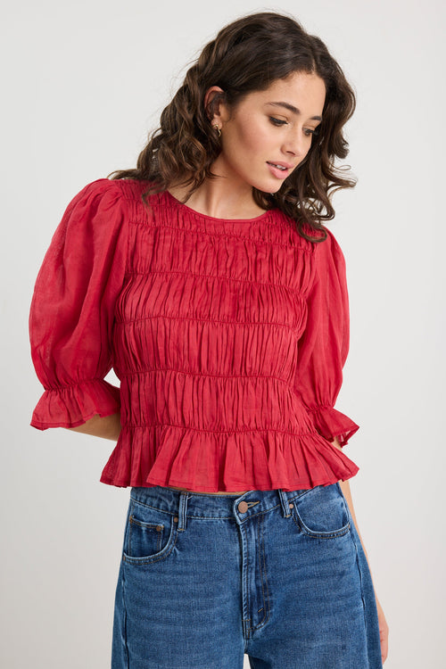Woman wearing a red blouse with puffed sleeves and blue jeans on a white background