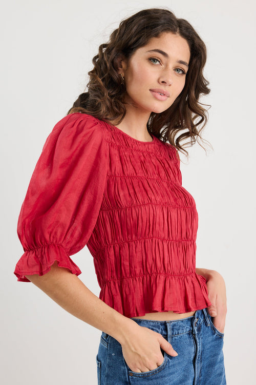 Woman wearing a red blouse with puff sleeves and blue jeans on a white background