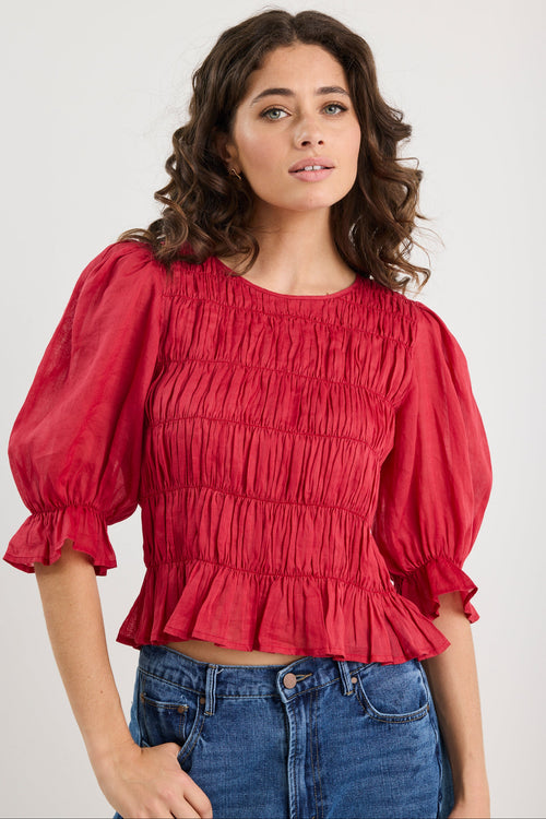 Woman wearing a red blouse with puffed sleeves and blue jeans on a white background
