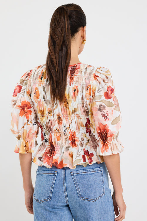 woman wearing a floral shirred short sleeve top with frill sleeves, styled with denim jeans and gold earrings.