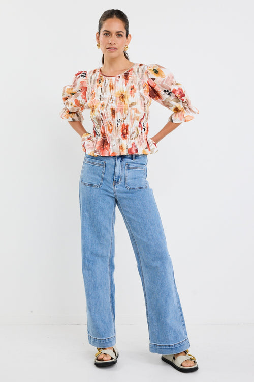 woman wearing a floral shirred short sleeve top with frill sleeves, styled with denim jeans and gold earrings.