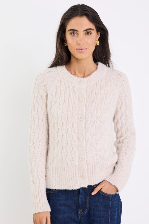 Woman wearing a cream cable knit cardigan against a white background