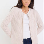 Woman wearing a beige cable knit cardigan over a white shirt with blue jeans on a white background