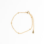 Gold bracelet with a teardrop charm on a white background