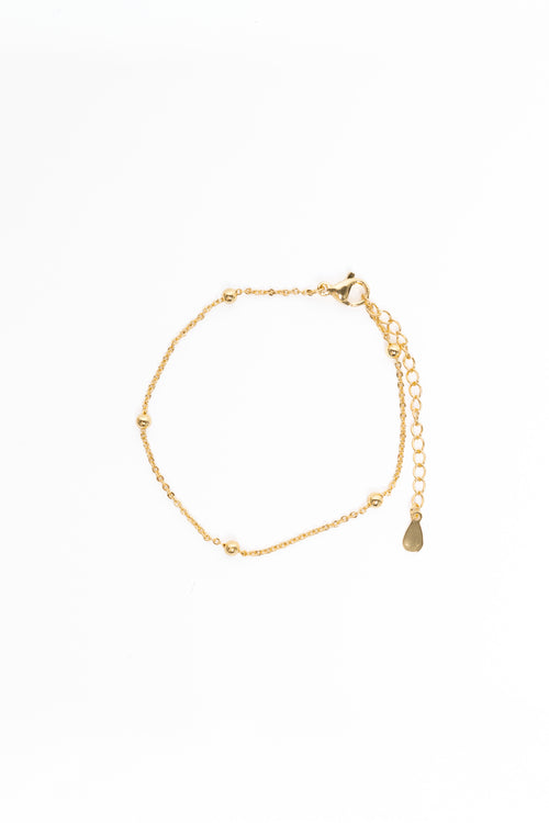 Gold bracelet with a teardrop charm on a white background