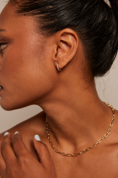 Model wears small diamante hoop earring with a gold chain necklace. 