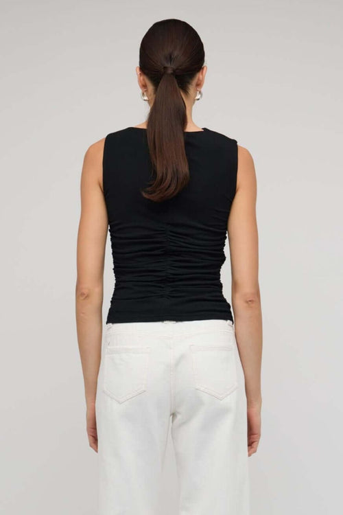 Black sleeveless top with asymmetric neckline and cutout detail, featuring a ruched body for a fitted silhouette, worn by a model against a neutral background.
