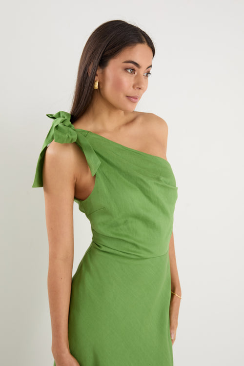 Model wears a one shoulder green midi dress with white heels