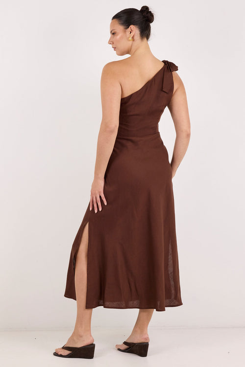 A woman modeling a brown one-shoulder midi dress with a side slit, shown from the back against a plain white studio background.