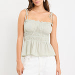 Woman wearing a sage green gingham strappy cami top with tie straps and an elasticated waist, styled with ecru jeans.