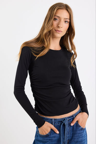 Woman wearing a black long-sleeve top and blue jeans on a white background