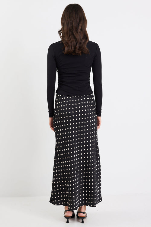 Woman wearing a black long-sleeve top and a long black and white patterned skirt on a white background