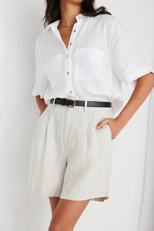 model wearing beige linen shorts and a white shirt