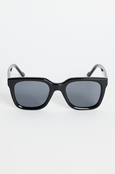 Glossy black rounded-square sunglasses with dark tinted lenses and RE:UNION label branding on the arm, photographed on a white background