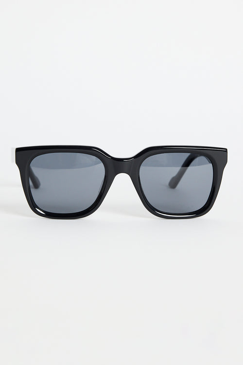 Glossy black rounded-square sunglasses with dark tinted lenses and RE:UNION label branding on the arm, photographed on a white background