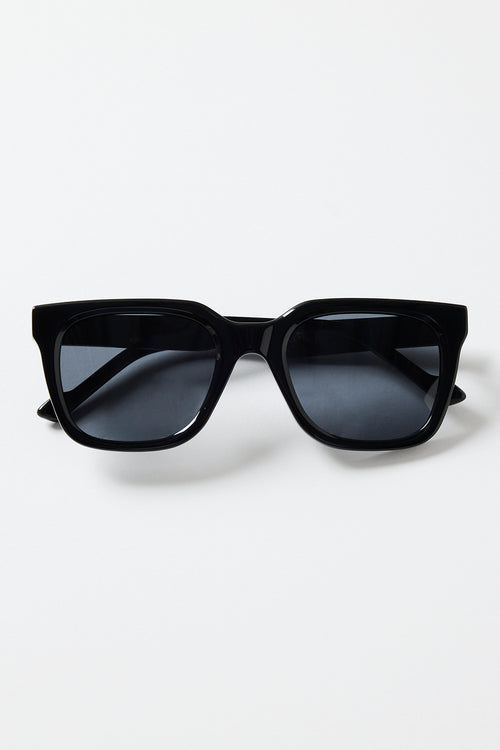 Glossy black rounded-square sunglasses with dark tinted lenses and RE:UNION label branding on the arm, photographed on a white background