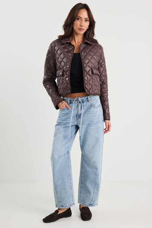 Woman wearing a quilted jacket, black top, and light blue jeans on a white background