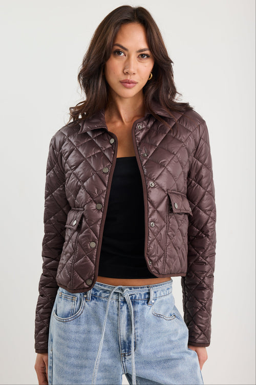 Woman wearing a quilted jacket, black top, and blue jeans on a white background